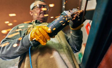 Yetişkin bir işçinin atölyesinde ürettiği yatay görüntü. Olgun marangoz erkek tamircide kıvılcımlar saçıyor..