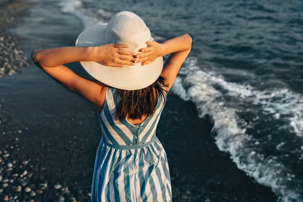 모자를 석양을 배경으로 해변을 아름다운 여인의 뒷모습을 자세히 들여다볼 수있다 — 스톡 사진