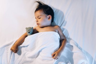 Geceleri beyaz yatakta uyuyan güzel bir kızın manzarasının üstünde. Küçük çocuk lamba ışığında odada şekerleme yapıyor. Evet. Küçük kız oyuncak bir ayıyla yatakta uyuyor.. 