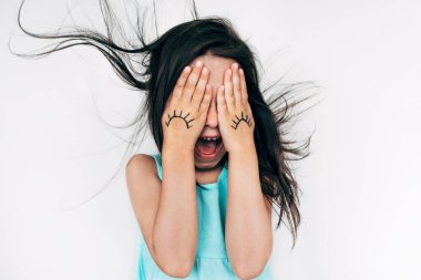 Şaşırmış küçük bir kızın portresi, ağzı açık ve saçlarını savurarak yüzünü buruşturuyor, iki eliyle gözlerini karalama gözleriyle kapatıyor. Çocuk eğleniyor ve peekaboo oynuyor. İyi eğlenceler..