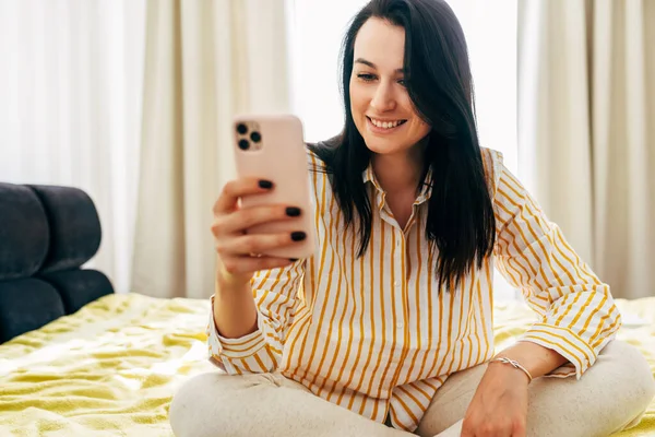 Happy Brunette Young Woman Sitting Bed Using Mobile Phone While Royalty Free Stock Images