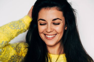 Çekici esmer kadının yakın çekimi sarı kazak giyiyor, saçlarına dokunuyor, kapalı gözlerle gülümsüyor, pozitif duygularla neşeleniyor, beyaz arka planda izole edilmiş.. 