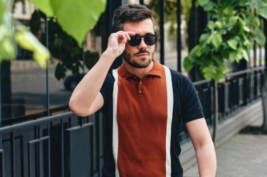 Açık havada, şık giyinmiş ve siyah güneş gözlüklü genç sakallı bir adamın şehir sokaklarında yürüyüşü. Hippi erkek, ortaklarıyla iş birliği yapmak için sokakta yürüyor..