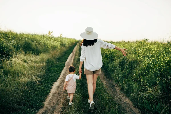 Anne ve kızının arka planda yürürken çekilmiş yatay dikiz görüntüsü. Dışarıda yürüyen bir kadın ve küçük tatlı bir kız. Annelik ve çocukluk kavramı.