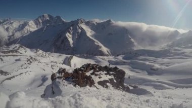 Bulutlar ve asansörler, güneş ışığı altında kar kaplı dağların arka planına doğru hareket eder.