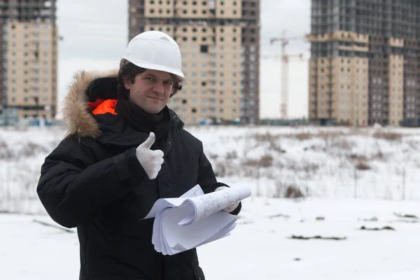 Engineer standing on the background of a new apartment building. House is built. Engineer in a helmet with papers in hand. The concept of new housing construction, real estate