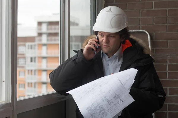 Yeni bir apartmanın arka plan üzerinde duran mühendis. Evi inşa edilmiştir. Gazetelerde el telefon ile bir kask mühendislik. Yeni konut inşaat, Emlak kavramı