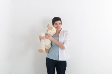 Öfkeli kadın ısır onu peluş oyuncak kedi kulak, gri studio arka plan için. Komik durum