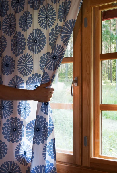 Hand opens curtain on the wooden cottage house window. Bright sunlight shines through. Beautiful summer morning light behind the window. — Stock Photo, Image