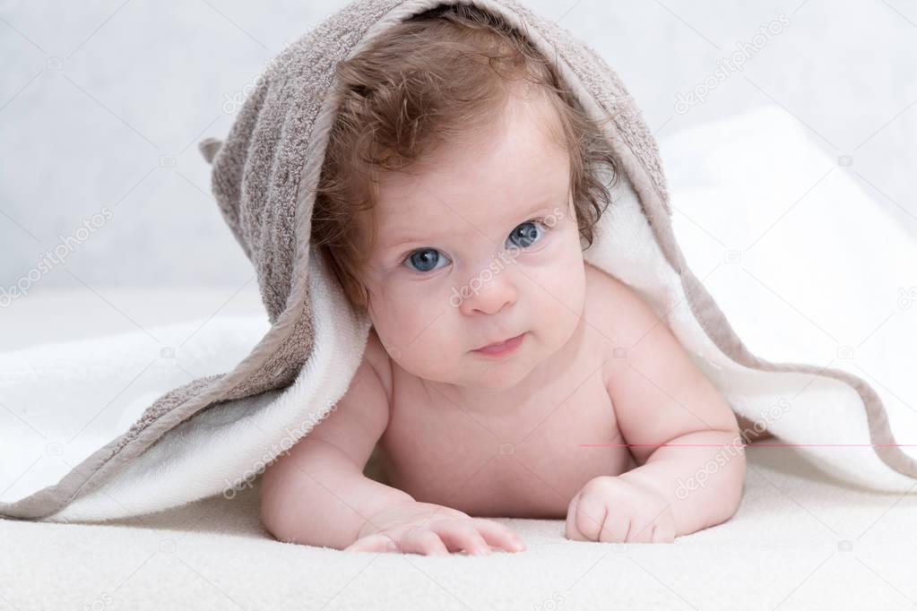 Cute newborn baby girl with beautiful blue eyes on a white terry coverlet. Adorable baby looking out under a white blanket or towel. Happy baby infant in towel after bathing in living room