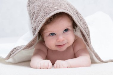 Kız bebek duş kafa havluya ile sonra gülümseyerek. Mutlu gülen bebek kapşonlu havlu banyodan sonra yatakta yatarken giyiyor. Temiz kuru çocuk yatak odasında. Banyo ve küçük çocuklara yıkama. Ararken.