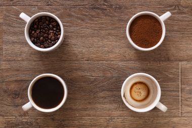 Bardak kahve ve kahve çekirdekleri eski ahşap masa üzerinde çeşitli. Dört fincan kahve, fasulye, zemin ve boş bardak içki - aşamaları.