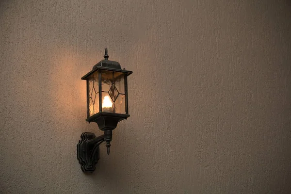 Uma lanterna de vidro amarelo pendurado em uma parede velha cinza. Lâmpada brilhante brilhante iluminando a parede de um edifício antigo — Fotografia de Stock
