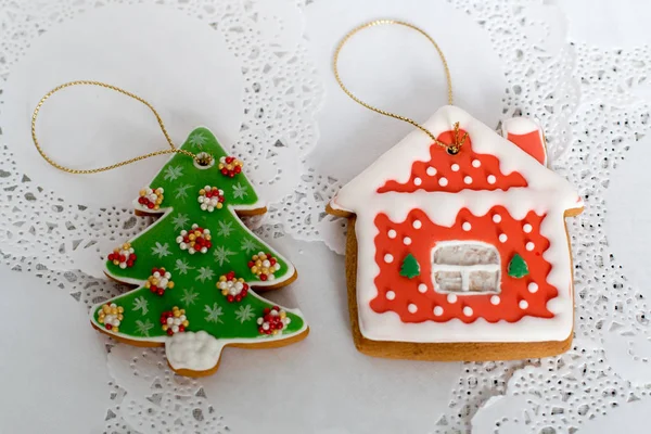 Two gingerbread cookies in the shape of the Christmas tree and small house on a white napkin background. Top view, flat lay, copy space.