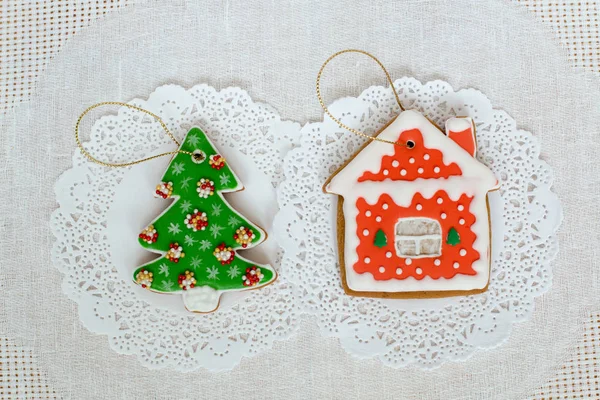 クリスマス ツリーと白いナプキン背景上の小さな家の形をした 2 つのジンジャーブレッド クッキー。フラット トップ ビュー レイアウト、コピー スペース. — ストック写真