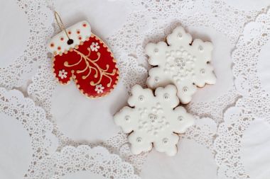 Kırmızı mitten ve beyaz peçete arka plan üzerinde iki kar taneleri şeklinde üç gingerbread çerezleri. Üstten Görünüm, düz yatıyordu, kopya alanı. Kıvırcık Noel gingerbread ev yemekleri.