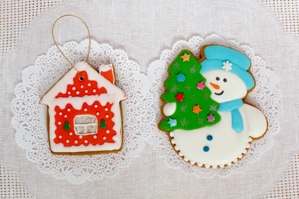 Два пряничных печенья в форме рождественской елки, снеговик и домик на белом фоне салфетки. Вид сверху, плоский, копировальное пространство . — стоковое фото
