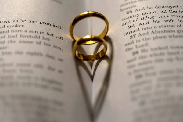 圣经上有两个结婚戒指 上面有心形的阴影 — 图库照片
