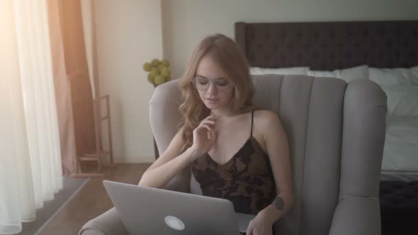 Linda mujer trabajando en su portátil mientras está sentada en un sillón en casa — Vídeos de Stock
