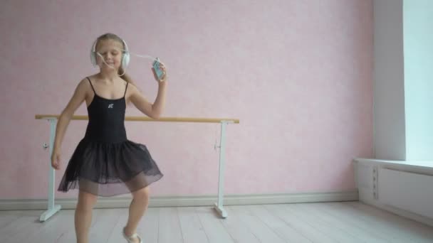 Happy little girl in ballet dress and headphones listening to music from smartphone and dancing — Stock Video