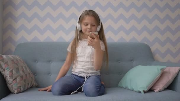 Kulaklığımda küçük kız evde kanepede otururken müzik smatphone dinliyor — Stok video