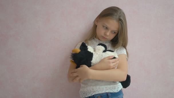 Сумна маленька дівчинка стоїть біля стіни з іграшкою — стокове відео