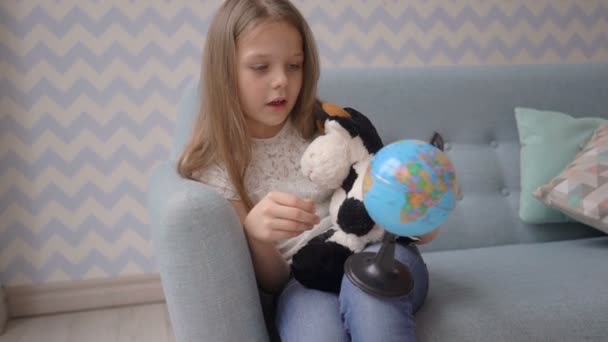 Linda chica sosteniendo y girar un pequeño globo mientras está sentado en el sofá en casa — Vídeo de stock