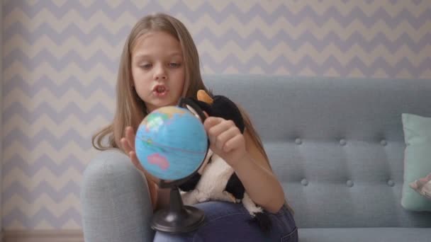 Симпатична дівчина тримає і обертає маленький глобус, сидячи на дивані вдома — стокове відео