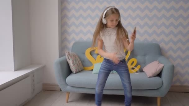 Gelukkig kind met hoofdtelefoons en smartphone dansen en muziek thuis beluisteren — Stockvideo