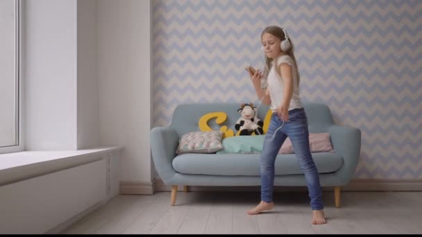 Niño feliz con auriculares y smartphone bailando y escuchando música en casa — Vídeo de stock