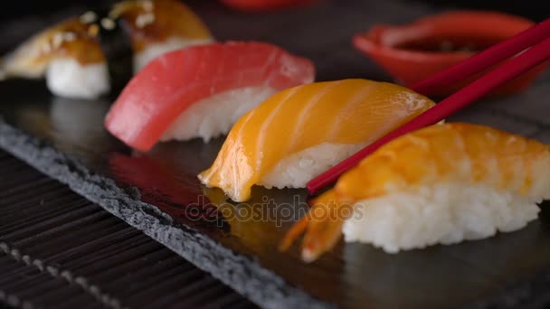 Palillos rojos tomando porción de rollo de sushi, comiendo rollo de sushi usando palillos — Vídeo de stock