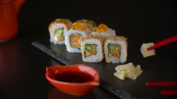 Hand met rode stokjes nemen roll sushi van donkere plaat — Stockvideo