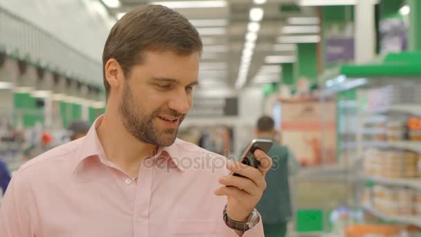 Веселий чоловік використовує мобільний телефон в магазині — стокове відео