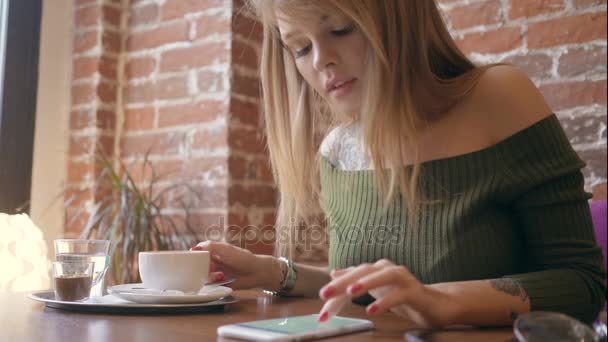 Joven mujer bonita bebiendo café y usando teléfono inteligente en la cafetería — Vídeos de Stock