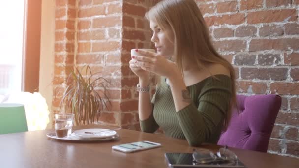 Hübsche junge Frau sitzt mit einer Tasse Kaffee im Café — Stockvideo