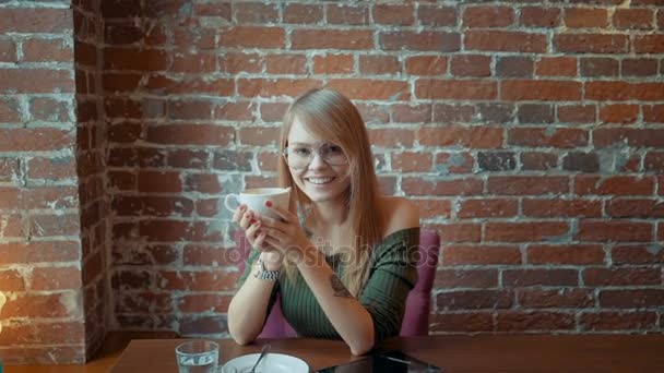 コーヒーのキャップ付きのカフェに座っているかわいい笑顔の女性 — ストック動画