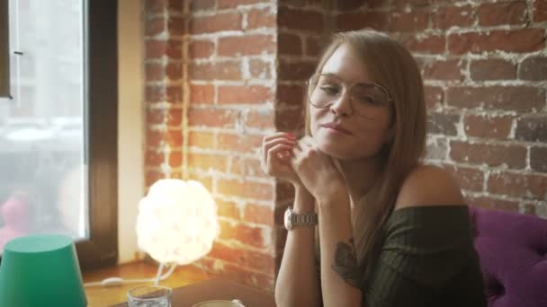 Niedlich lächelnde Frau sitzt in einem Café gegen Backsteinmauer — Stockvideo