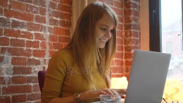 Bella studentessa con sorriso carino tastiera qualcosa su net-book, bella donna felice che lavora sul computer portatile durante la pausa caffè nel bar del caffè — Video Stock