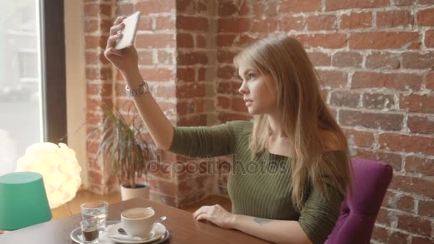 Mulher bonita está fazendo selfie usando um telefone inteligente e sorrindo enquanto descansa no café — Vídeo de Stock