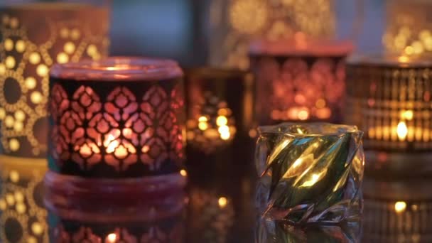 Разнообразие огней свечей с отражением на стеклянном столе вечером — стоковое видео