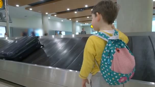Criança esperando sua bagagem na correia transportadora no lounge de chegadas do prédio do terminal do aeroporto — Vídeo de Stock