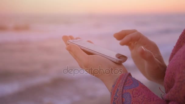 女性のホールドと使用してフレア光と海の背景にモバイル . — ストック動画