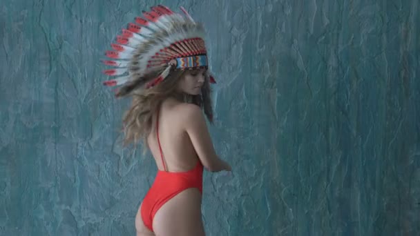 Sexy model in red swimsuit with native American headdress posing in studio — Stock Video