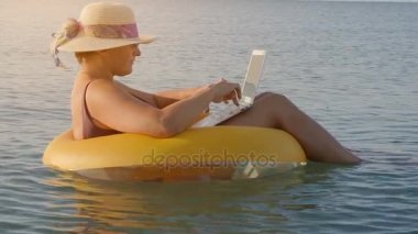 Kadın serbest meslek denizde şişme bir yüzüğü oturan bir dizüstü bilgisayarda çalışır,