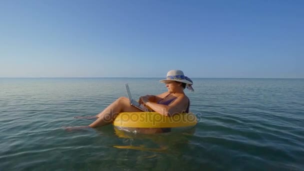 Mujer de mediana edad trabajando en computadora portátil en anillo de vida inflable naranja en vacaciones — Vídeos de Stock
