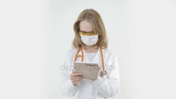 Doctora joven con máscara y estetoscopio usando tableta — Vídeos de Stock
