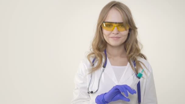 Молода жінка лікар посміхається і тримає шприц на білому тлі — стокове відео