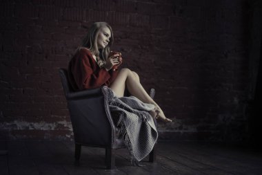 Kırmızı koltukta oturan ve rahatlatıcı elinde kahve fincan ile kazaklı genç kız