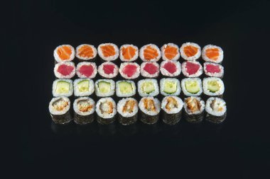 Büyük suşi ruloları siyah arka planda servis edilir.