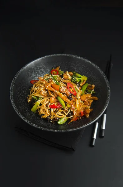 Tagliatelle asiatiche con pollo, verdure in ciotola nera e bacchette. Stile di cibo asiatico — Foto Stock